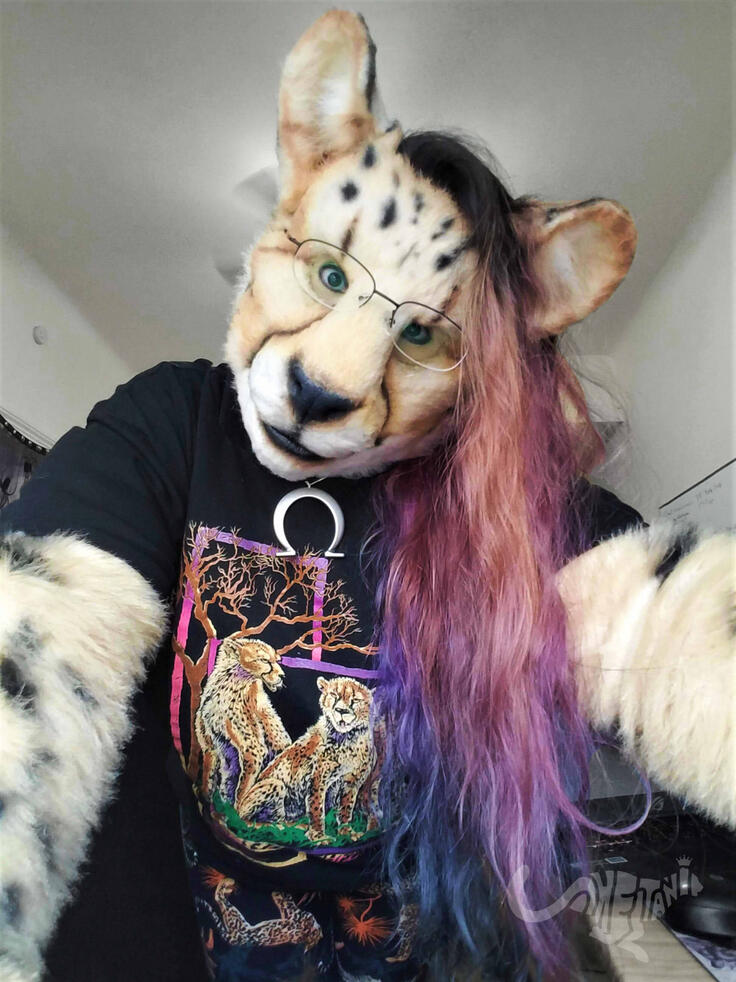 Shetani leaning over the camera, her hair dyed in an orange/pink/blue fade to match the colors in her vintage 1990s shirt