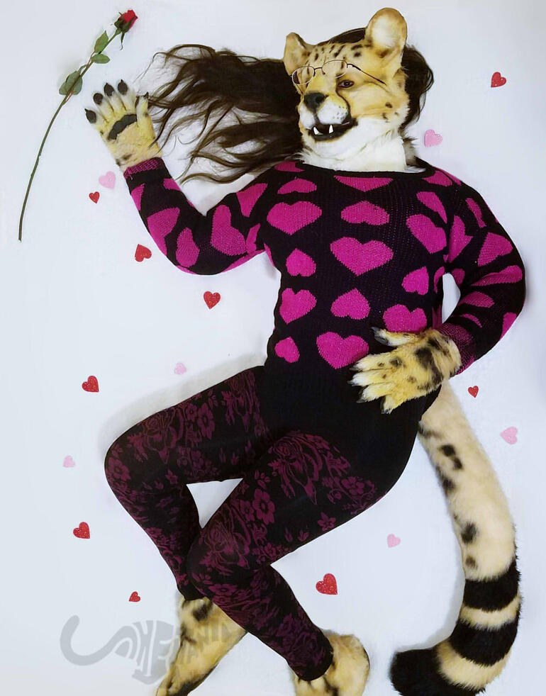 Shetani lying on a white sheet with her hair spread out beneath her, reaching for a rose, surrounded by hearts.