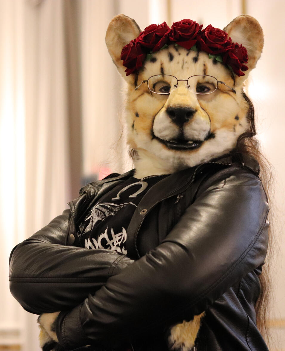 Closeup on Shetani with her arms crossed, wearing the leather jacket and flower crown