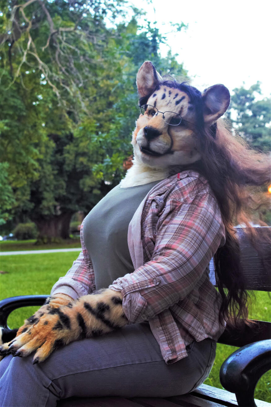Shetani sitting on a park bench looking off into the distance, hair blown by the wind