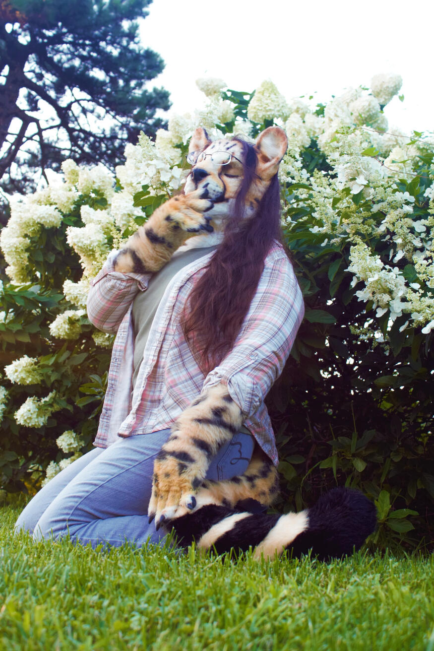 Shetani in a park, kneeling in front of a bush of big white flowers with her eyes closed. Soft lighting