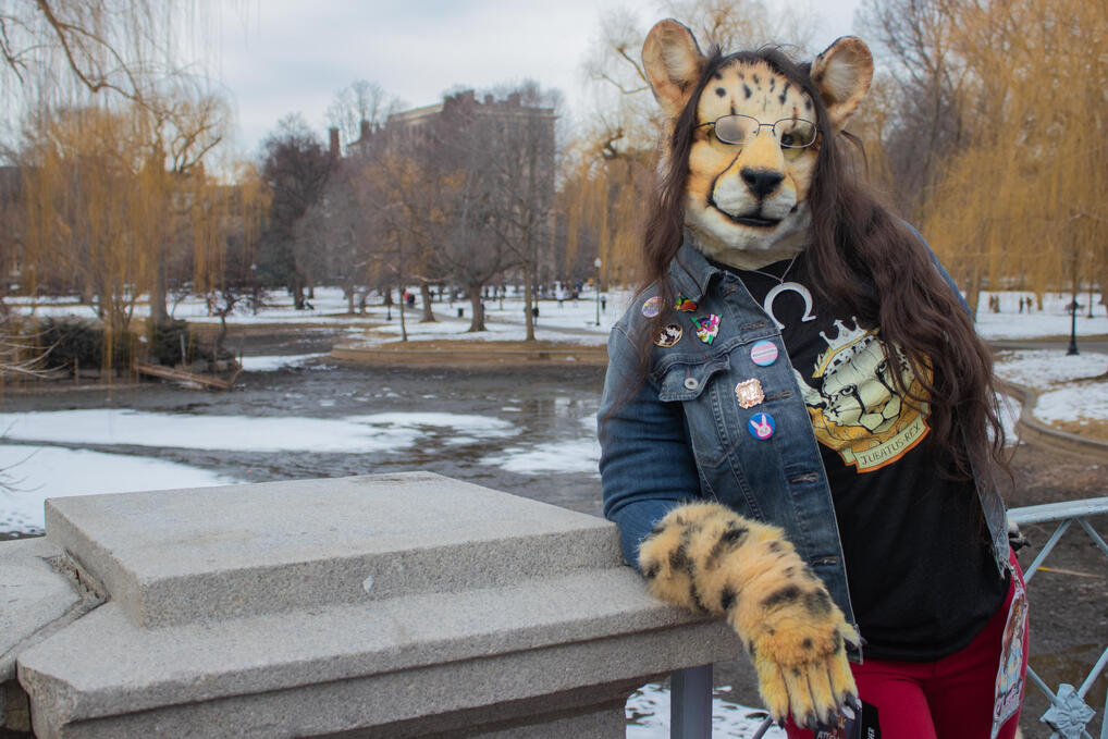Shetani leaning on a bridge railing overlooking a frozen pond. Her breath fogs her glasses. Jacket front shows pins and buttons Shetani leaning on a bridge railing overlooking a frozen pond. Her breath fogs her glasses. Jacket front shows pins and buttons
