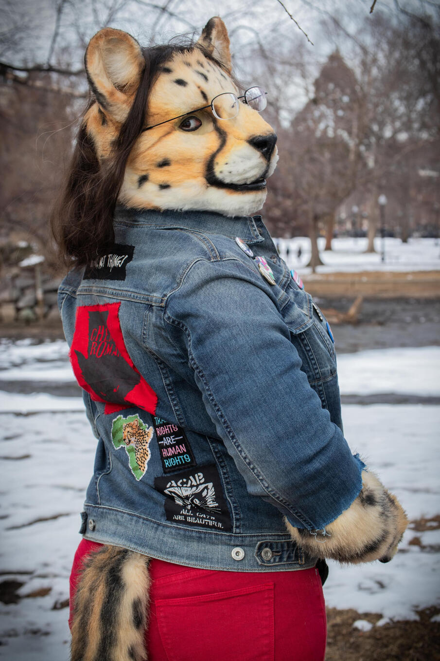 Snowy winter park. Looking back over her shoulder at the viewer, the back of Shetani&#39;s denim jacket is adorned with patches