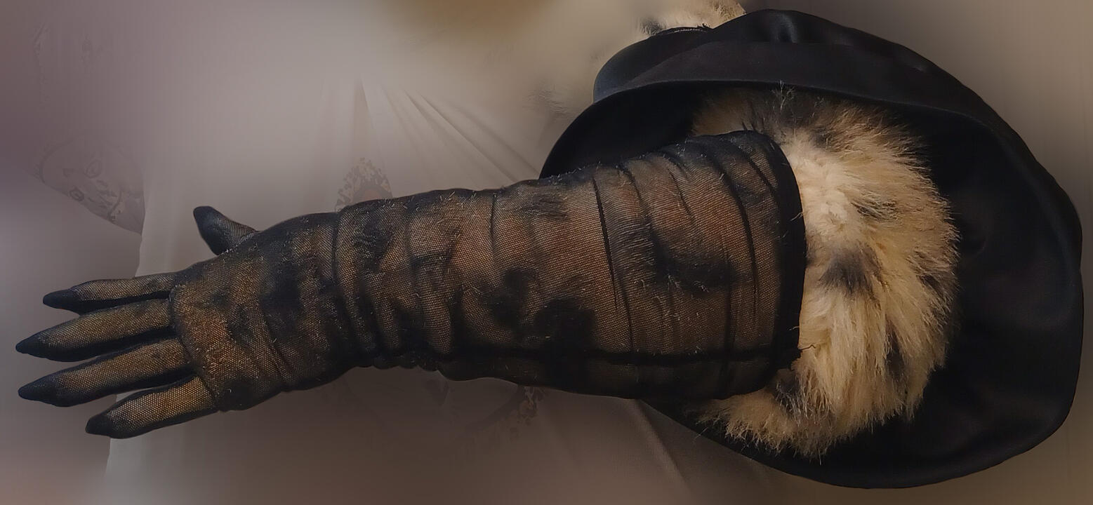 Highlighted, Shetani's arm modeling an elbow-length fishnet opera glove and large puffy black bell sleeve around the bicep. Fluffy cheetah fur protrudes from the area between the two, and the spots are visible through the glove's fabric.