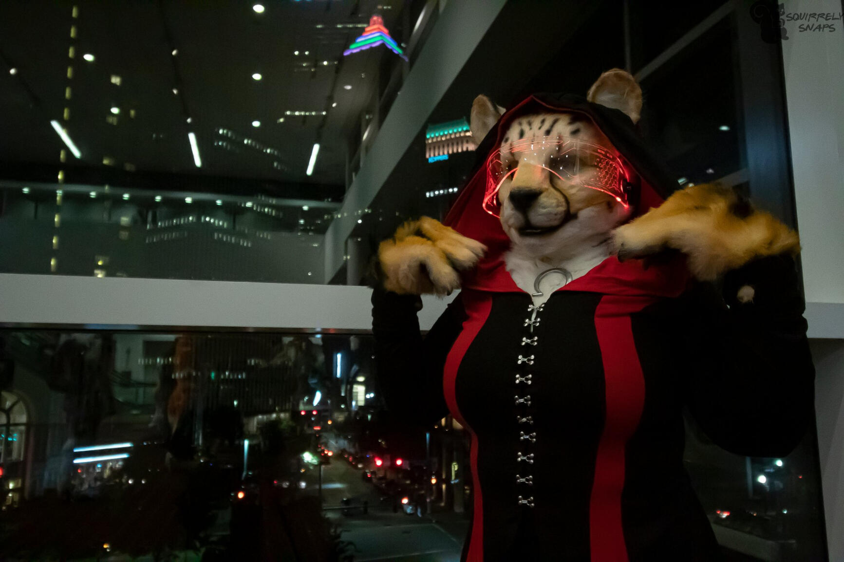 Shetani pulling on the hood of her black and red-striped cyberpunk cloak. The window behind shows a city at night