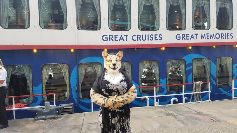 Shetani in fursuit standing in front of the cruise ship, about to board