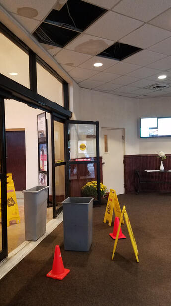 Falling ceiling tiles and a garbage can to catch the ceiling leak in front of the automatic doors. Big wet puddle on carpet