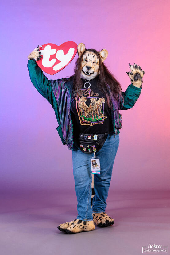Shetani posing in a 1990s themed outfit with an oversized cardboard Beanie Baby ear tag