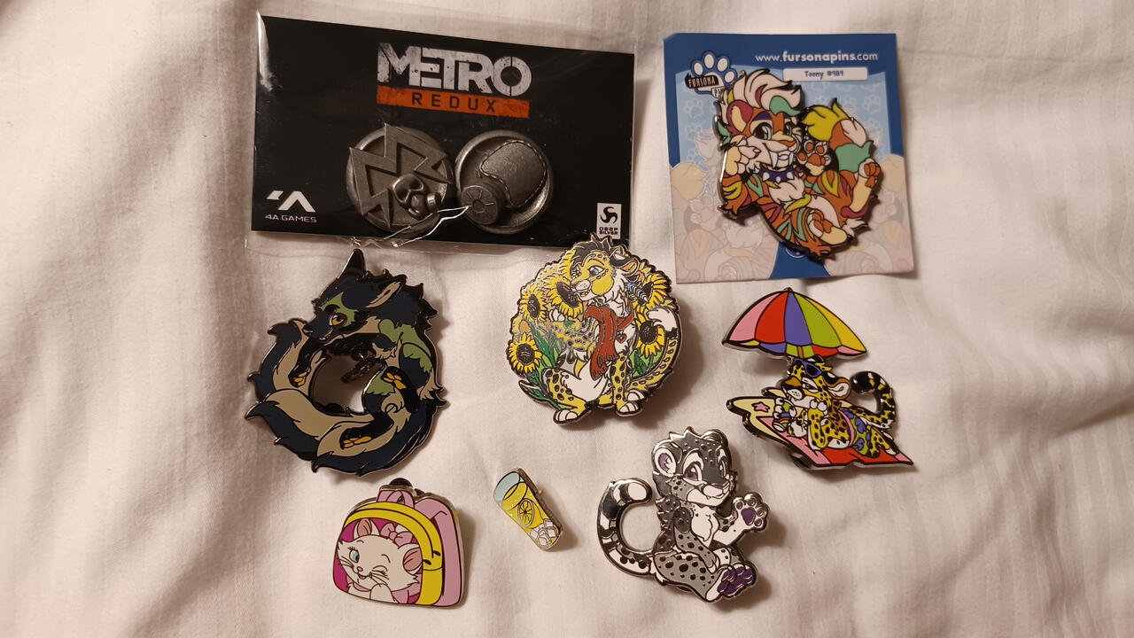 Enamel pin haul, including a Metro Redux set, Fursona Pins asexual cheetah, vacation cheetah, and cheetah with sunflowers, Marie from the Aristocats, a tiny glass of lemonade, Fursona Pins fox and tiger