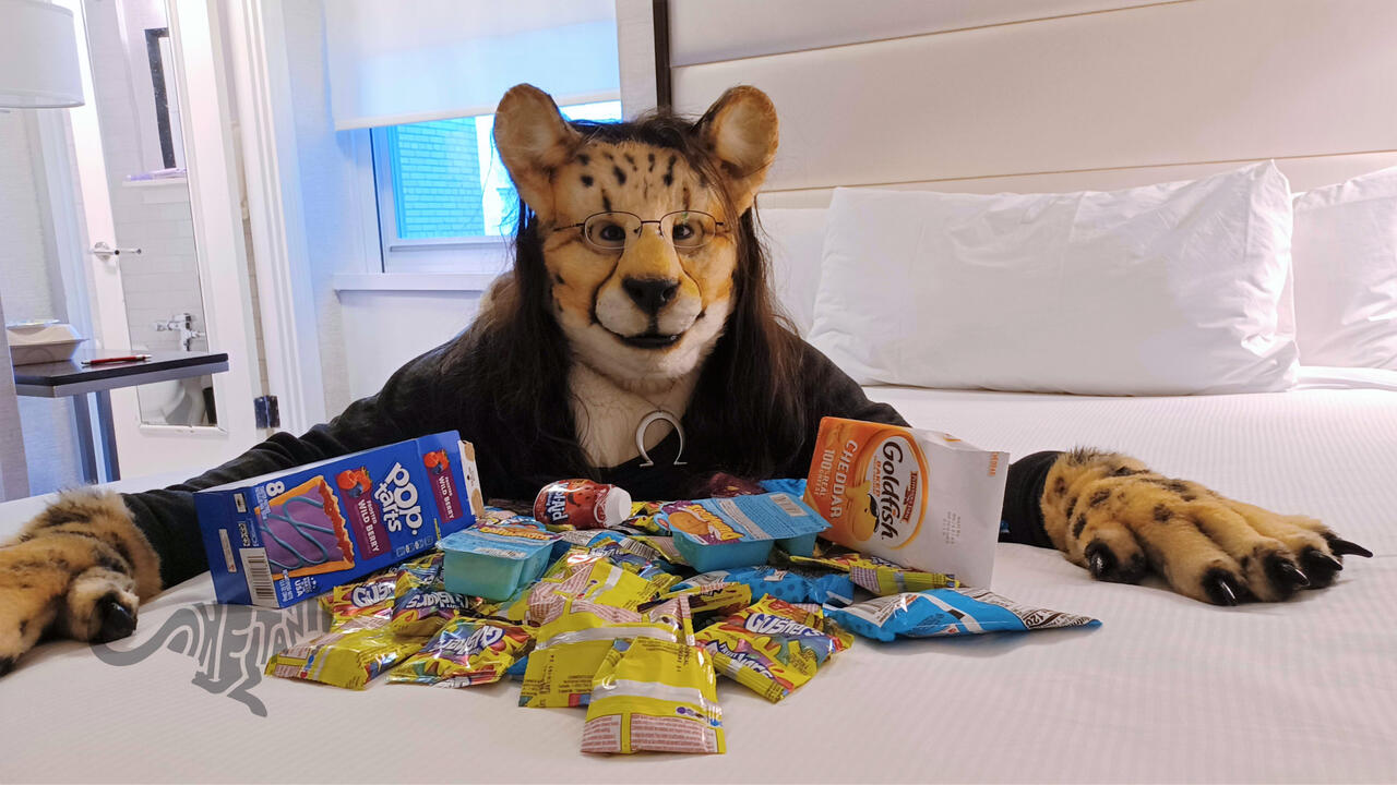 Shetani on a bed with a pile of Gushers, Dunkaroos, and other 1990s snacks