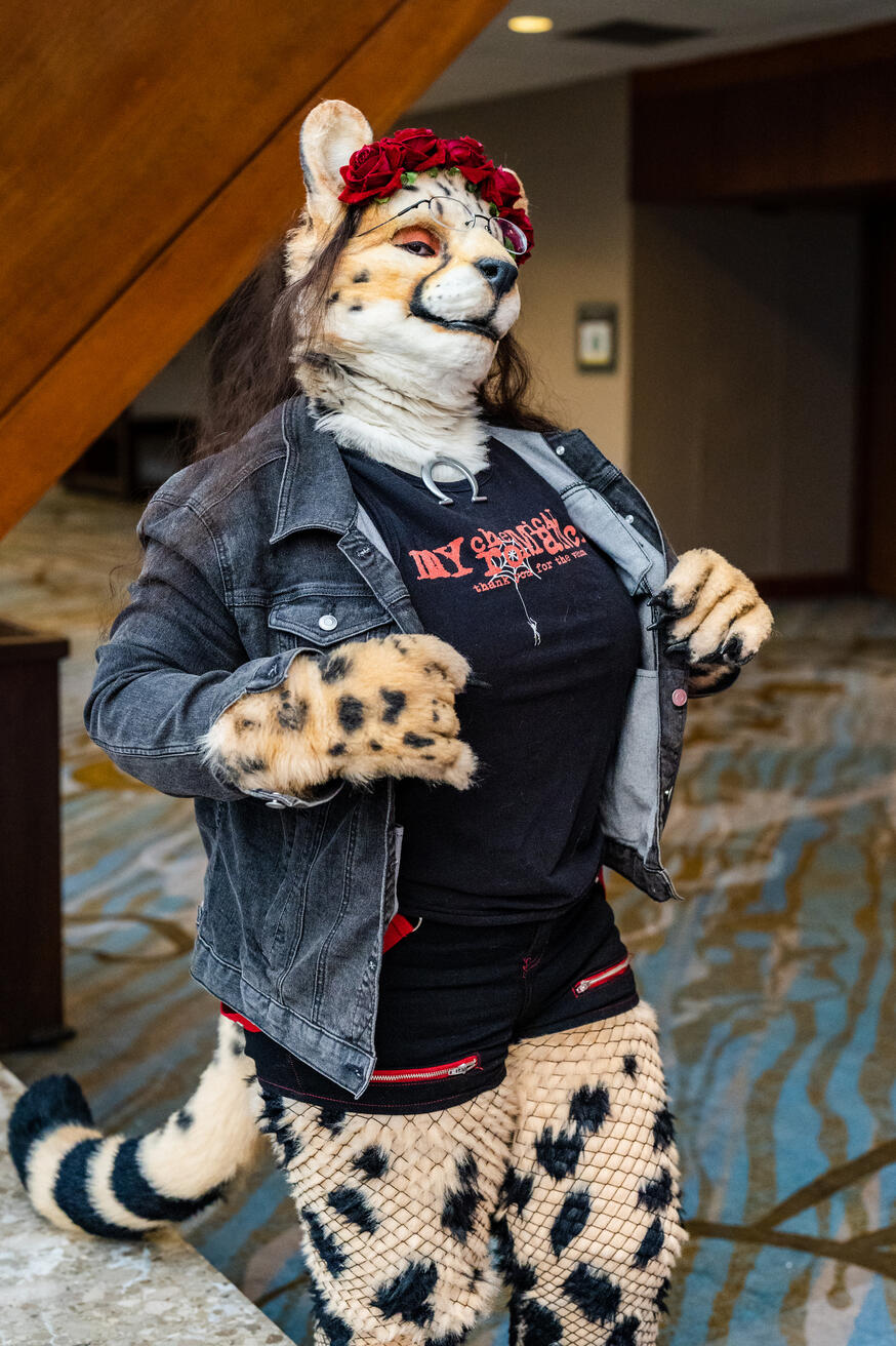 Shetani proudly popping the lapels on her denim jacket, head cocked. Natural lighting highlights the red eye makeup matching her flower crown and accents in her punk rock outfit