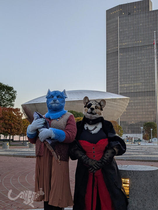 Mika looking skyward, off into the distance; Shetani glaring haughtily down at the camera with both paws on her cane. The Egg looms large behind them.