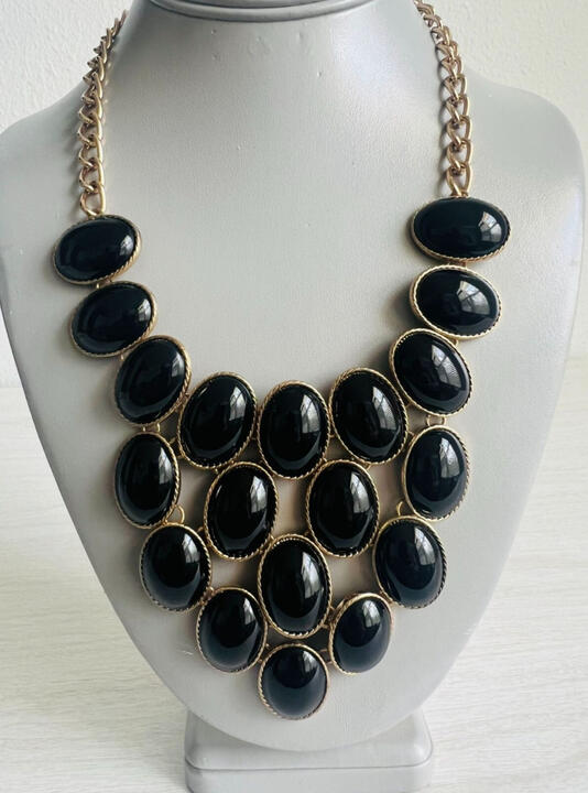Product photo of a costume-jewelry necklace, large bib of black oval cabochons set in gold attached to a gold chain.