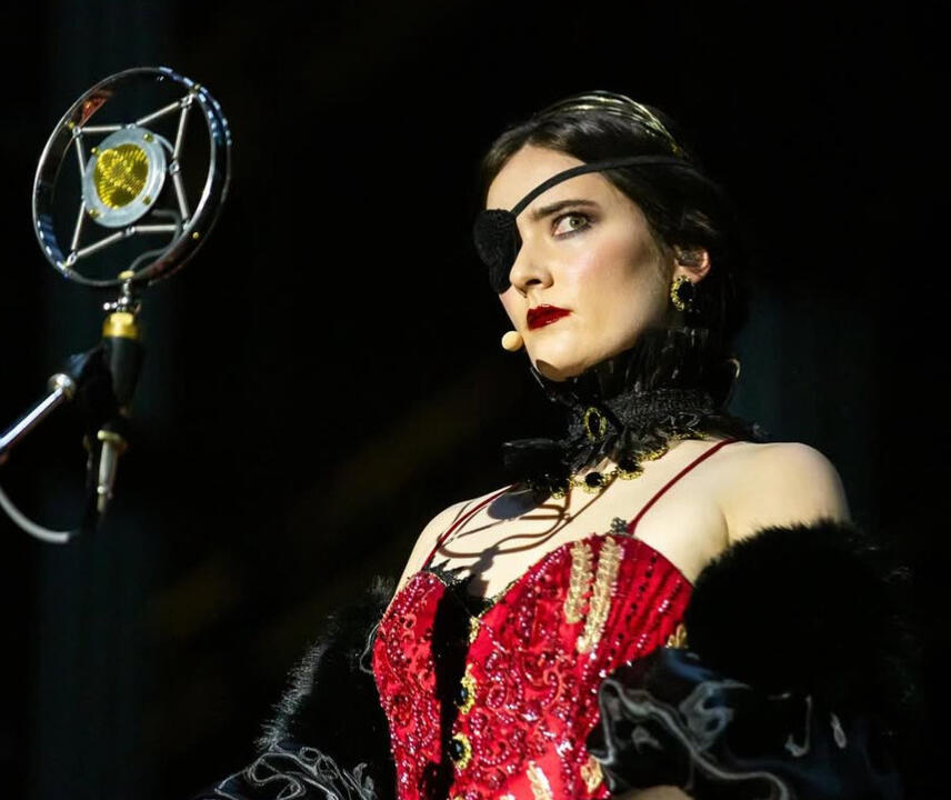 Close-up photo of Sylvia, a stern-looking opera singer dressed in opulent red and black, wearing an eyepatch.