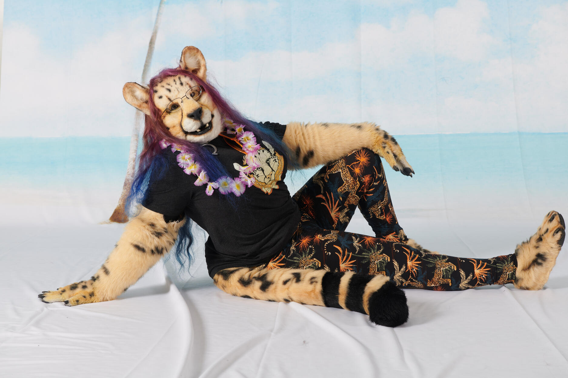 Convention photobooth picture, beach backdrop, Shetani is wearing a t-shirt with tropical cheetah leggings and a flower lei